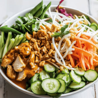 Gezonde poke bowl met verse groenten, kip in pindasaus, knapperige noten en kruiden, geserveerd op een witte houten tafel.